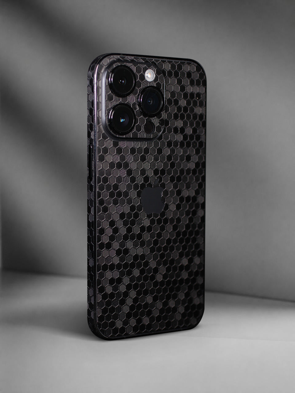 A black honeycomb-patterned iPhone Vinyl Skin photographed in a studio setting with a gray background.