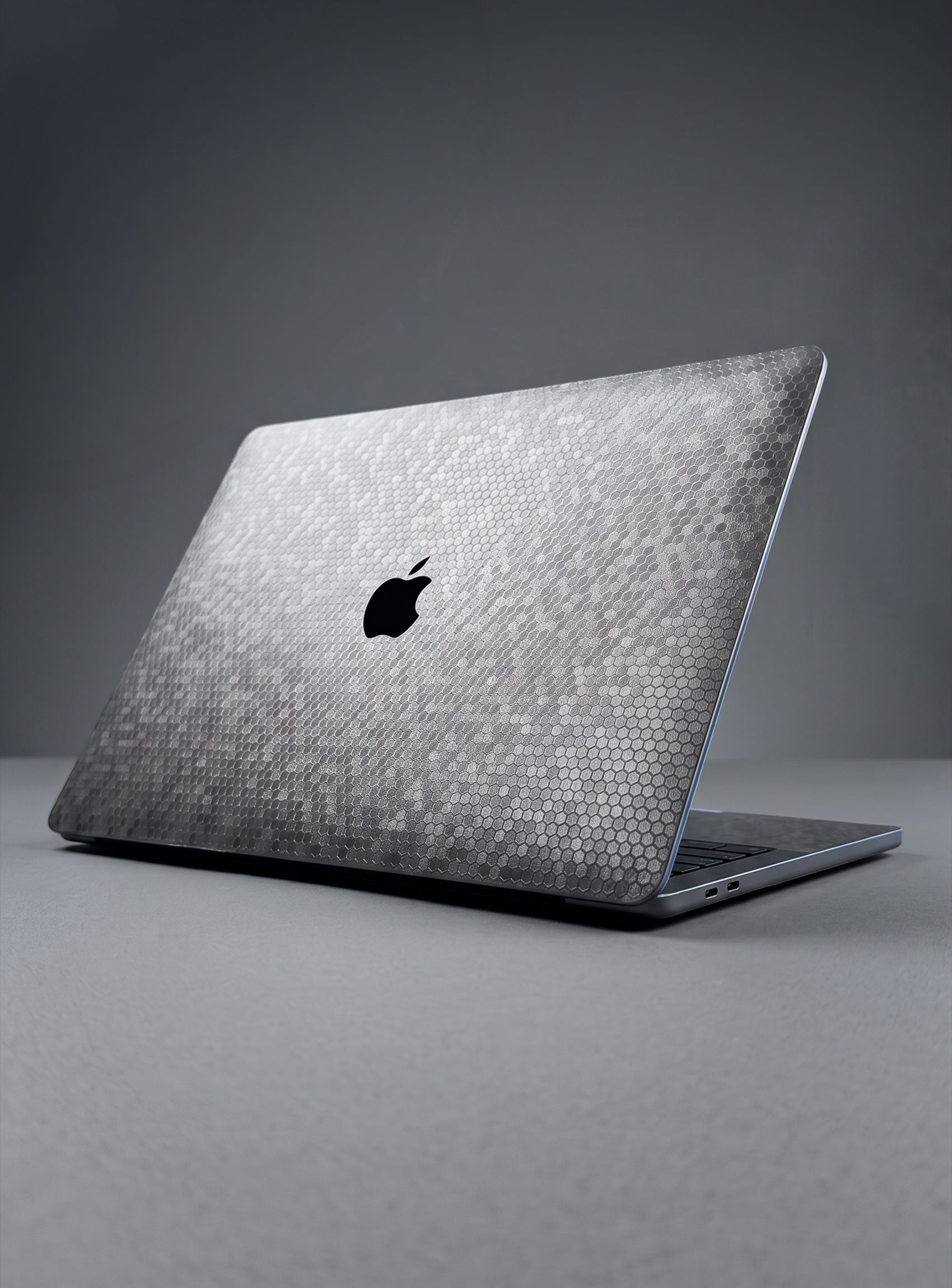 A Apple MacBook laptop with a textured, metallic honeycomb-patterned skin on the lid, show on a dark gray studio background.