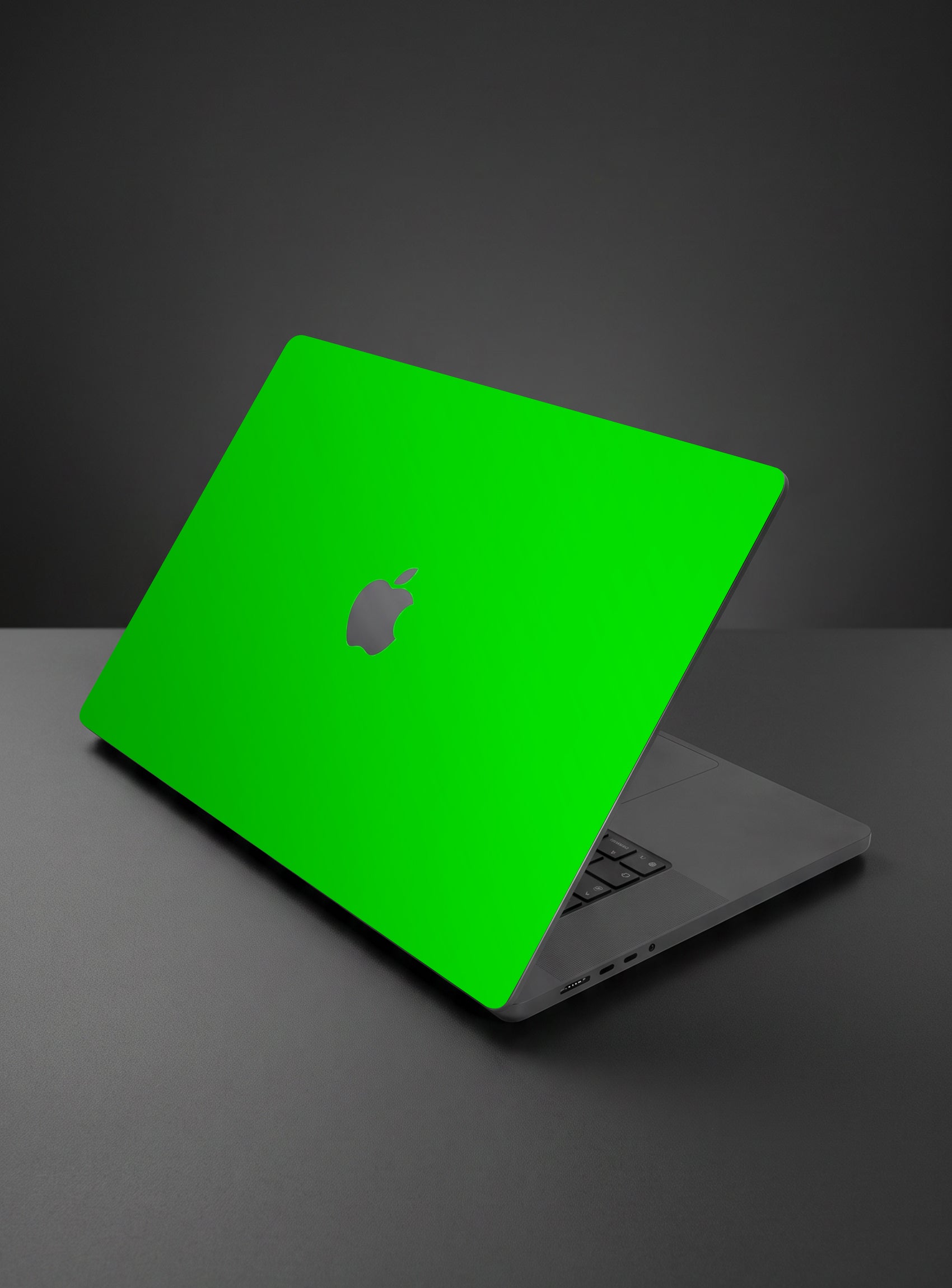 A apple macbook laptop with a bright neon green protective skin or decal on the lid, shown open on a dark gray surface against a dark gray background.