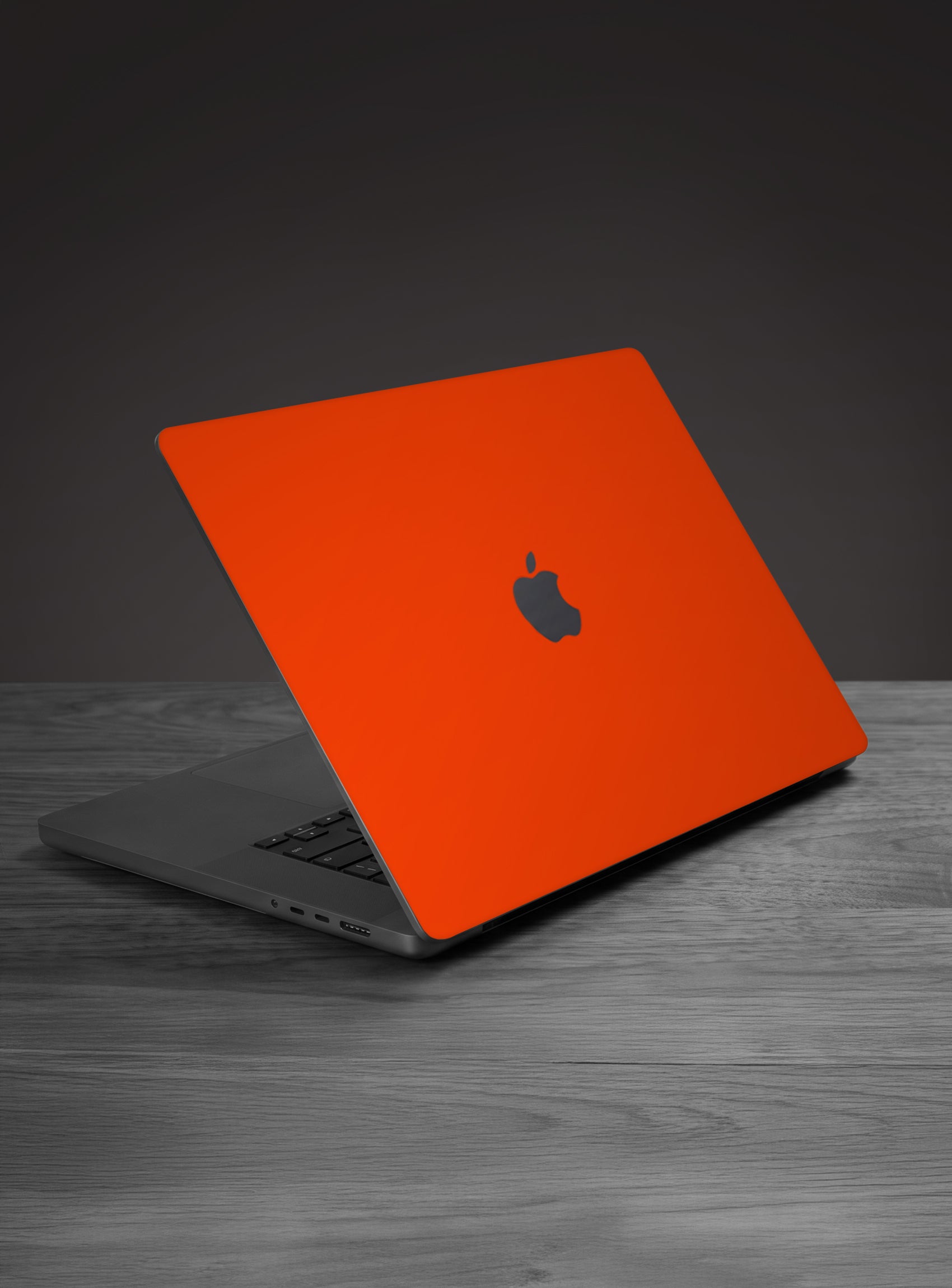 A apple macbook laptop with a bright orange protective skin or shell on its lid, placed on a gray wooden surface against a dark gray background.