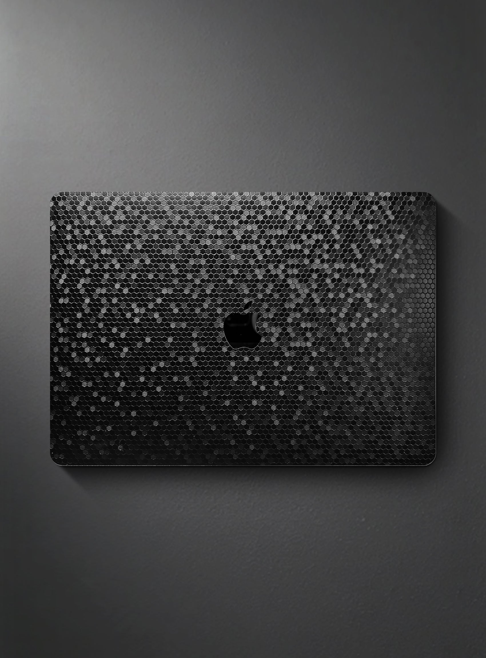 A black honeycomb textured apple macbook laptop skin or decal, featuring a honeycomb pattern and a cutout for the Apple logo, shown on a dark gray background.