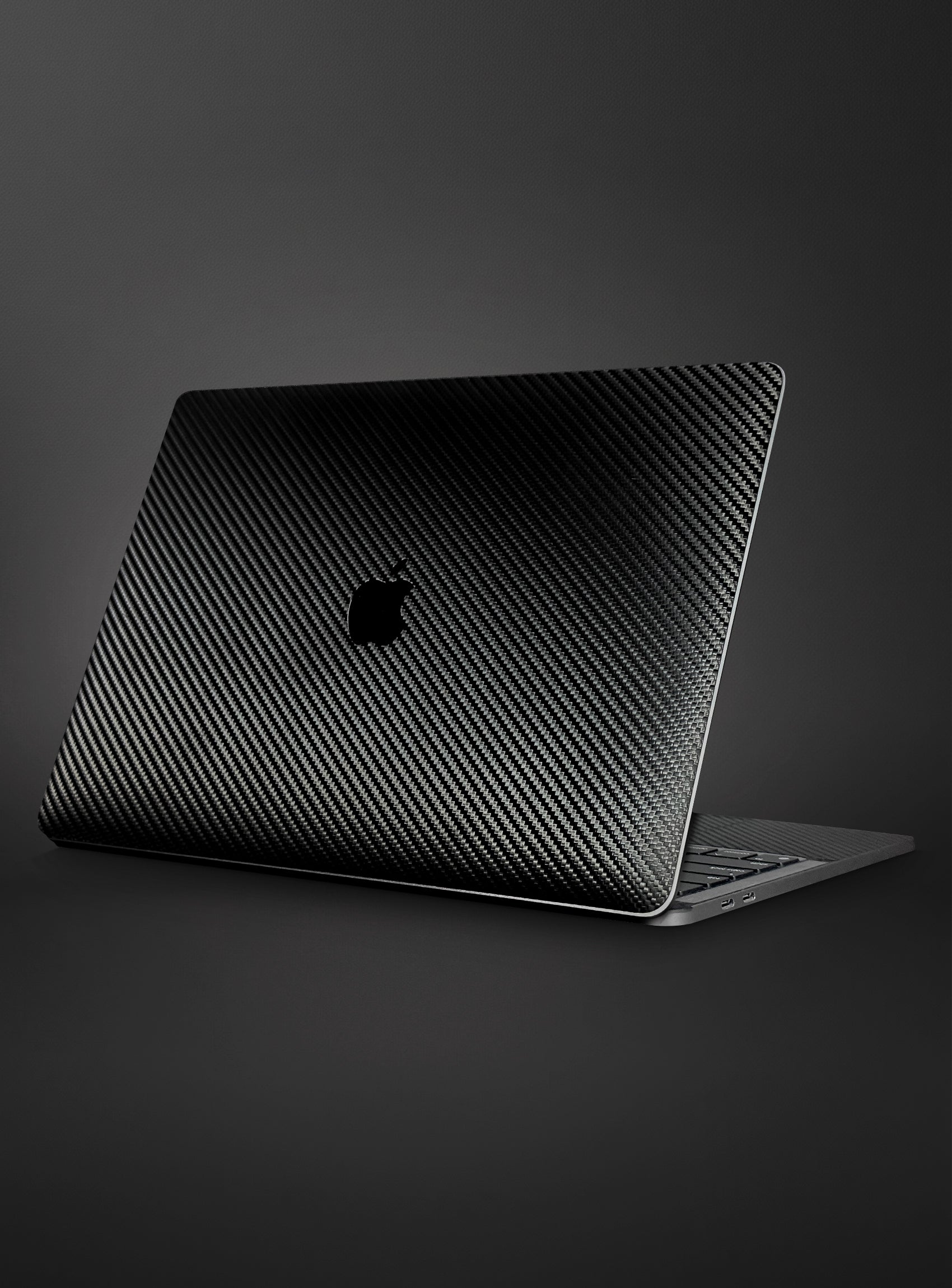 A apple macbook laptop with a black carbon fiber textured skin on its lid, shown on a dark gray background.